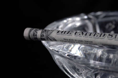 A dollar shaped like a cigarette resting on an ashtray.の写真素材