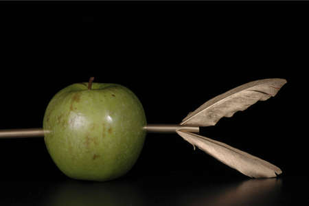 A green apple pierced by a golden arrow agaisnt a black background.の写真素材
