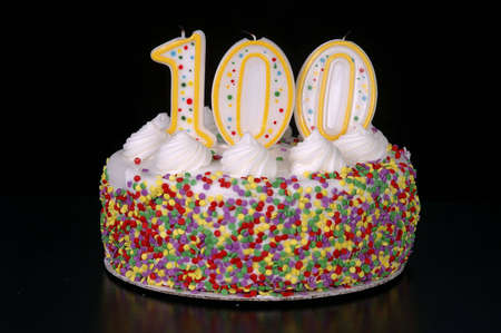 A colorful birthday cake with candles shaped like the number 100. Black background.の写真素材