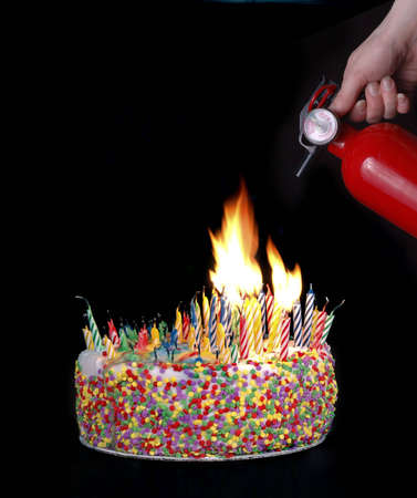 A hand holding a fire extinguisher above a cake with candles creating a fire.の写真素材