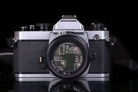 A circuit board can be seen in the lens of a mechanical film camera. Black background.