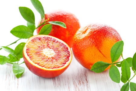 Several blood oranges with leaves,whole and halved on a wooden tableの写真素材
