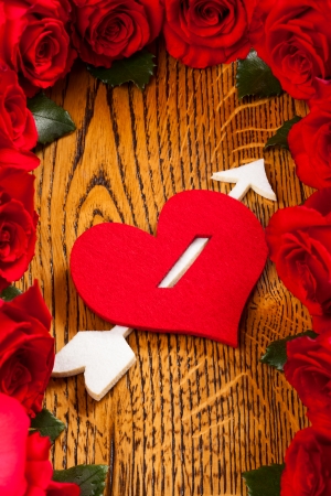 heart pierced by  cupid arrow and red roses on the wooden backgroundの写真素材