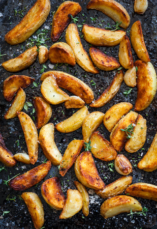 Roasted potato wedges with herbs and garlic on a baking trayの写真素材