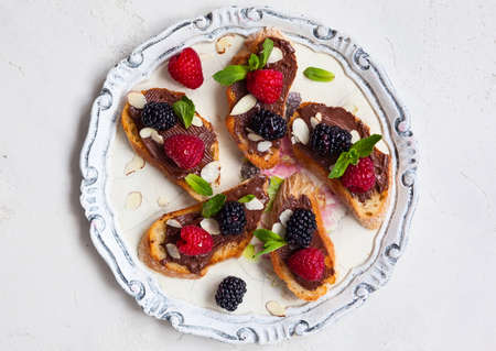 Sweet berry bruschetta with chocolate nut butter,mint and sliced almonds on the white vintage dishの写真素材