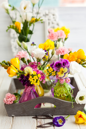 Beautiful fresh flowers in glass bottles on the wooden tableの写真素材