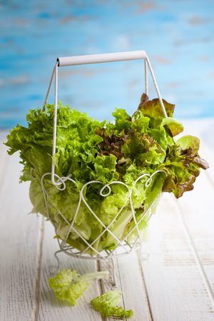 Various types of lettuce in a basket on the wooden tableの写真素材