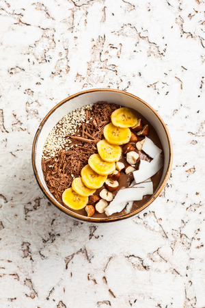 Chocolate hazelnut smoothie bowl topped with sliced banana, shredded coconut, chopped  chocolate, nuts and sesame seeds.の写真素材