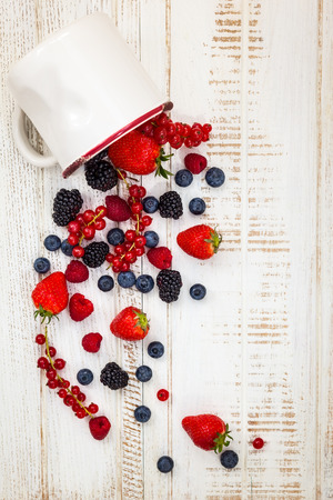 Fresh summer berries in vintage mug over wooden backgroundtop viewの写真素材