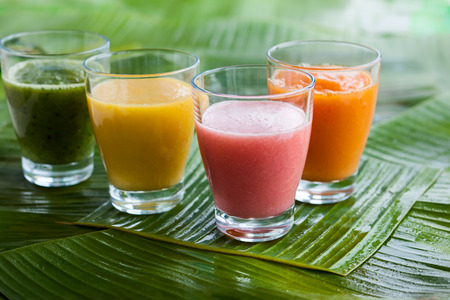 Assortment of fresh  tropical fruits smoothies on the green banana leavesの写真素材