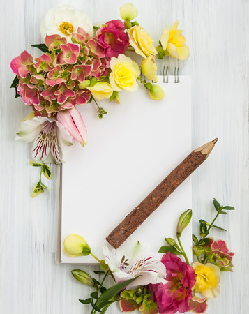 Blank notepadpen and flowers over white wooden background. Top view with copy spaceの写真素材