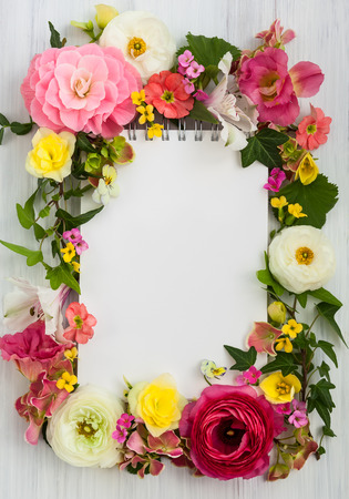 Blank notepad and flowers over white wooden background. Top view with copy spaceの写真素材