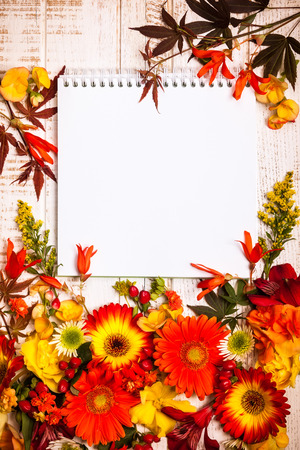 Blank notepad and autumnal flowers  on vintage wooden background. Top view with copy spaceの写真素材