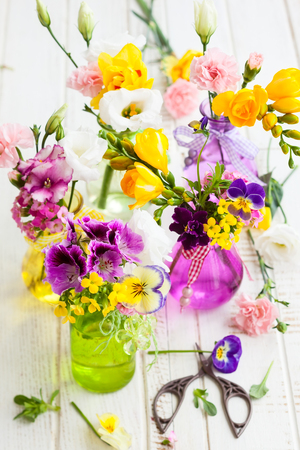 Beautiful fresh flowers in glass bottles on the wooden table