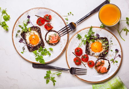 Fried eggs on slices of whole grain bread, salmon canape and baked cherry tomatoesの写真素材