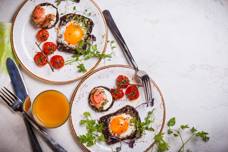 Fried eggs on slices of whole grain bread, salmon canape and baked cherry tomatoesの写真素材