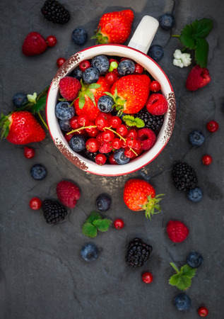 Fresh summer berries in vintage mug over black background,top viewの写真素材