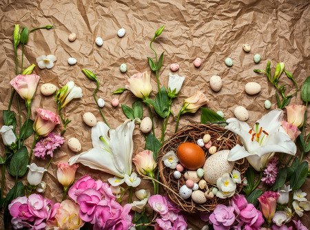 Easter composition with festive flowers decoration and traditional treats : easter chocolate candy mini eggs in bird nest. Top view with copy spaceの写真素材