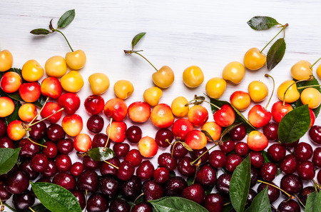 Assorted of fresh ripe cherry with green leaves on the white wooden.の写真素材