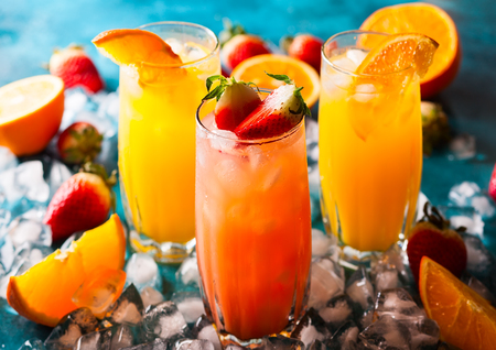 Different types of summer drinks in glasses, cubes of ice and slice of fruits  on blue table. Healthy vitamin fruit and berry drinks.の写真素材