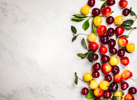 Assorted of fresh ripe cherry with green leaves on the old light background. Top view, copy spaceの写真素材