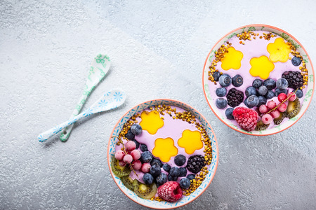 Smoothie in bowls for healthy breakfast. Berry yogurt with blueberries,raspberry,blackberry,red currant, mango, kiwi  and bee pollen over grey background. Top view, copy spaceの写真素材
