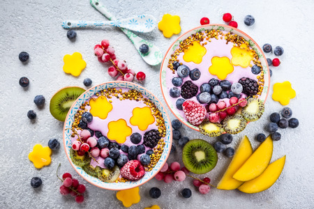 Smoothie in bowls for healthy breakfast. Berry yogurt with blueberries,raspberry,blackberry,red currant, mango, kiwi  and bee pollen over grey background. Top view, copy spaceの写真素材