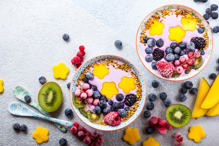 Smoothie in bowls for healthy breakfast. Berry yogurt with blueberries,raspberry,blackberry,red currant, mango, kiwi  and bee pollen over grey background. Top view, copy spaceの写真素材