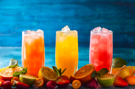 Different types of summer drinks in glasses, cubes of ice and slice of fruits  on blue table. Healthy vitamin fruit and berry drinks.の写真素材