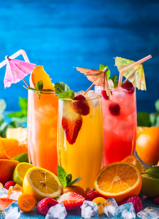 Different types of summer drinks in glasses, cubes of ice and slice of fruits  on blue table. Healthy vitamin fruit and berry drinks.の写真素材
