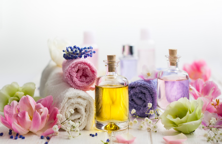 Bottles with essential aroma oil,towels different colors and fresh flowers  on white wooden background. Spa concept. Healthy cosmetic care. Place for textの写真素材