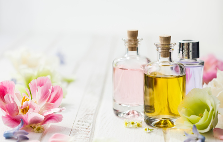 Bottles with essential aroma oil and flowers on white wooden background. Healthy skin care. Place for text.の写真素材