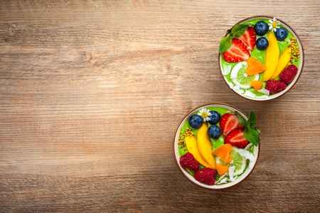 Green Smoothie in bowls for healthy breakfast. Fresh organic smoothie made from spinach, banana, spirulina,wheatgrass and lime with berries and fruits on wooden background.Top view, copy spaceの写真素材