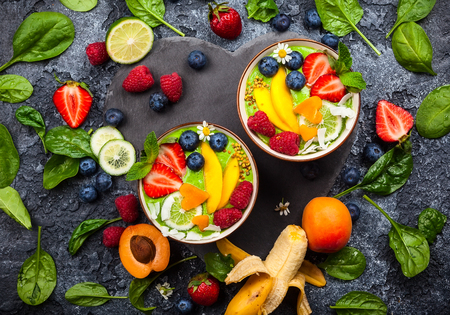 Green Smoothie in bowls for healthy breakfast. Fresh organic smoothie made from spinach, banana, spirulina,wheatgrass and lime with berries and fruits on black background.Top view, copy spaceの写真素材