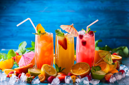 Different types of summer drinks in glasses, cubes of ice and slice of fruits  on blue table. Healthy vitamin fruit and berry drinks.の写真素材