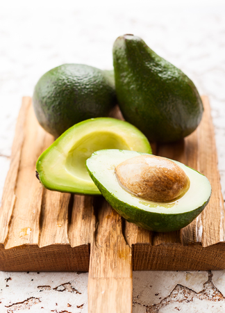 A whole and a halved avocado on wooden boardの写真素材
