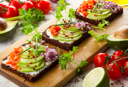 Fresh vegetarian open sandwiches on black bread with avocado, tomato and red onion on the wooden board. Concept healthy eatingの写真素材