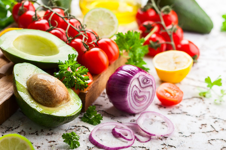 Fresh raw vegetable ingredients for healthy cooking. Avocado, cherry tomatoes, citrus and fresh herbs on wooden cutting board and tableの写真素材