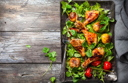 Spicy roasted chicken legs with potatoes and salad. Top view. Food in rustic style.の写真素材