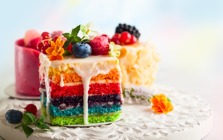 Various slices of cakes on a white tray: rainbow cake, raspberry cake and almond cake. Sweets...