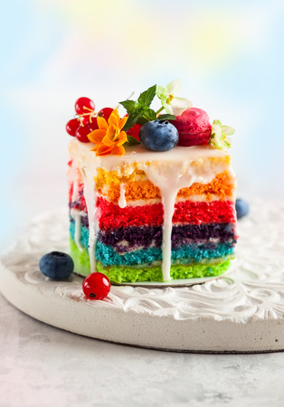 A slice of rainbow cake decorated with fresh berries and flowers for holidayの写真素材