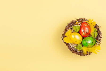 Easter composition with colorful Easter eggs in nest on yellow background. Easter card with copy space. Top view.の写真素材