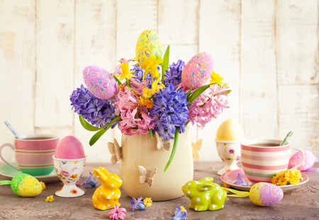 Easter breakfast table with tea, eggs in egg cups, spring flowers in vase and Easter decor.