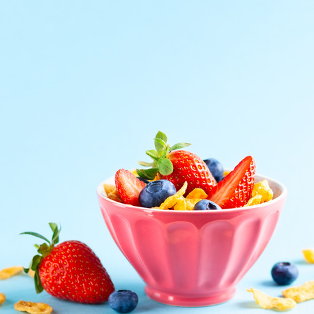 Concept of healthy gluten free breakfast with berries,natural yogurt and corn flakes in the pink bowl on blueの写真素材