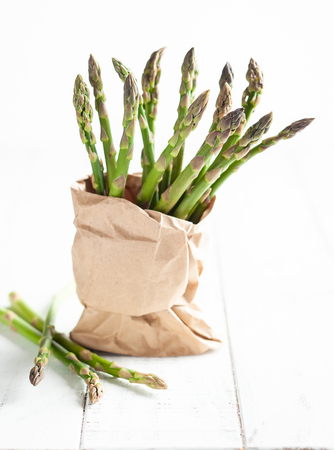 A bunch of green asparagus in paper bag on a white wooden table.の写真素材