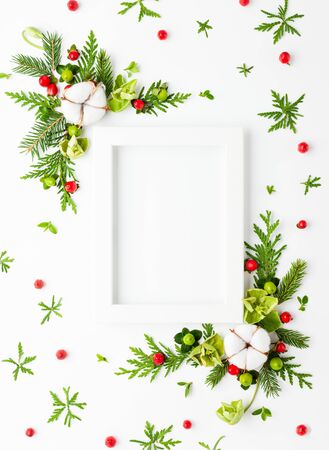 Christmas composition  with photo frame, cotton flower, branches of spruce and holly with red berries on white background. Merry christmas greeting card with empty space for holiday text. Flat layの写真素材