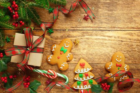 Christmas background with gift box, gingerbread cookies, branches of holly and fir on wooden background. Winter festive concept. Flat lay, copy space.の写真素材