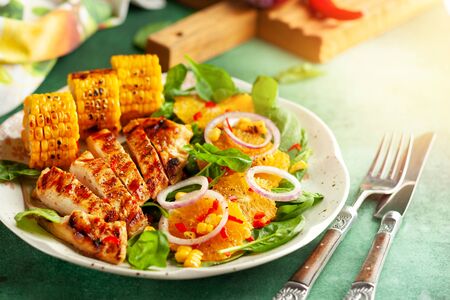 Grilled chicken breasts cooked on a BBQ served with citrus salad and corn on a plate. Close up view. Concept homemade summer dinnerの写真素材