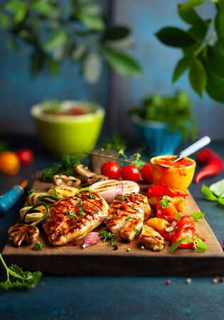 Grilled chicken breasts and different vegetables ad mushroom cooked on a BBQ served on wooden board. Close up view. Concept homemade summer barbeque dinnerの写真素材