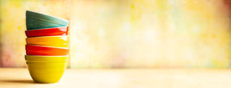 Kitchen cooking utensils background with ceramic multi- colored bowls on yellow background. Concept of home kitchen decor. Front view, copy space.の写真素材